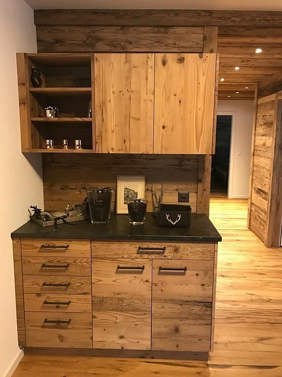 Küchenschränke aus Holz mit dunkler Arbeitsplatte, Oberschränke mit offenen Regalen und einem Eingang zu einem anderen Raum.