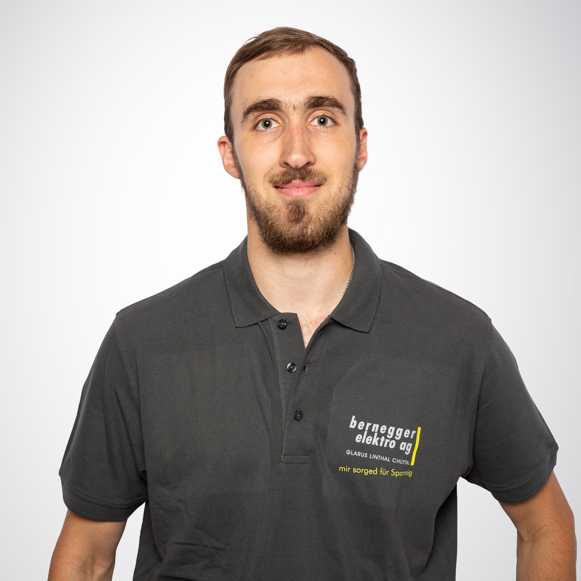 Mann trägt ein graues Poloshirt mit Firmenlogo, lächelt in die Kamera, weißer Hintergrund.