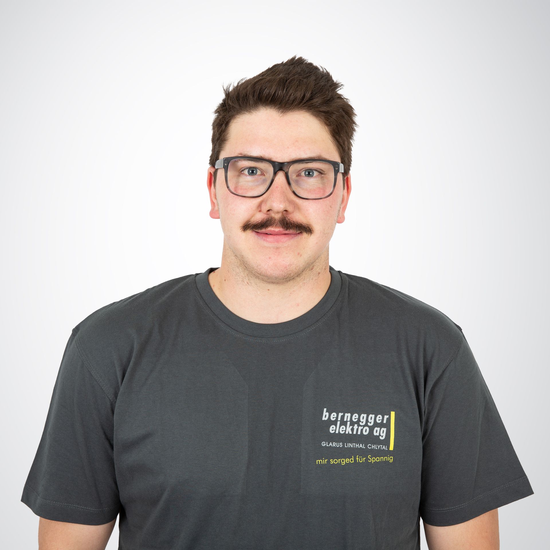 Mann mit Schnurrbart, Brille und grauem T-Shirt mit dem Logo „Bernegger Elektro AG“.