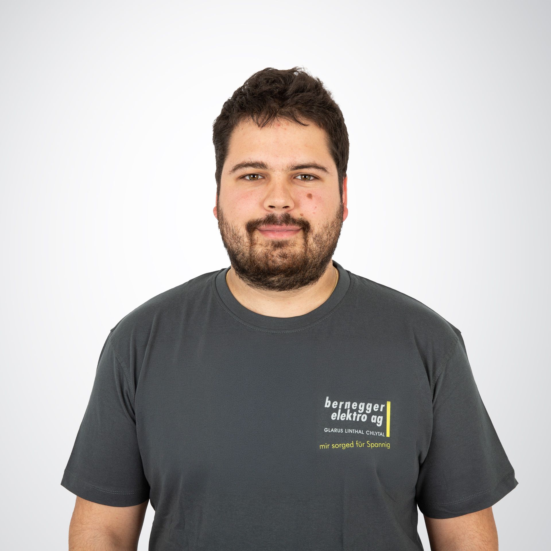 Mann mit Bart und grauem T-Shirt mit dem Logo „Berggogger Elektre AS“. Posiert im Innenbereich vor weißem Hintergrund.