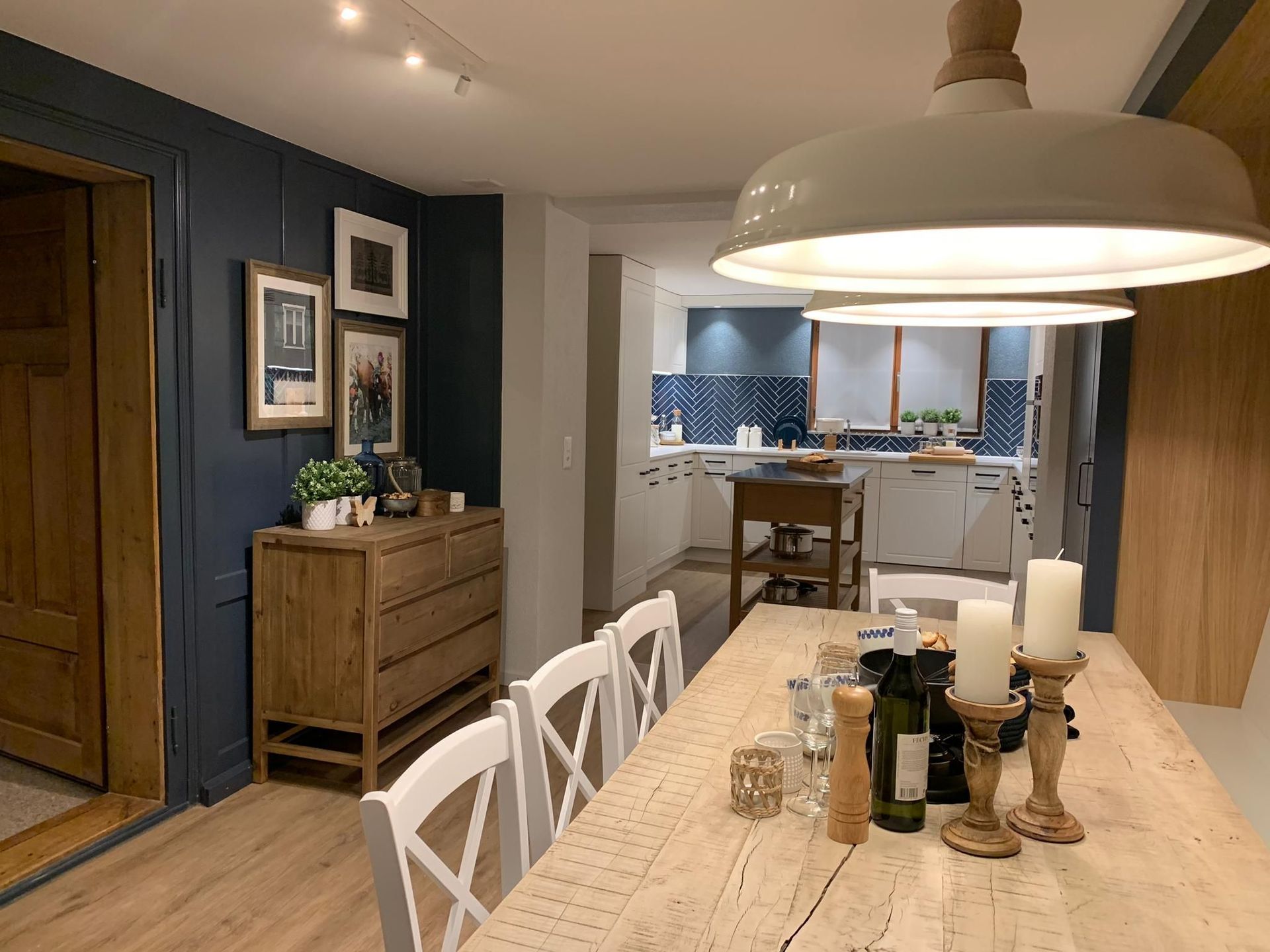 Gemütliches Esszimmer mit einem langen, für eine Mahlzeit gedeckten Holztisch, der zu einer Küche mit weißen Schränken und