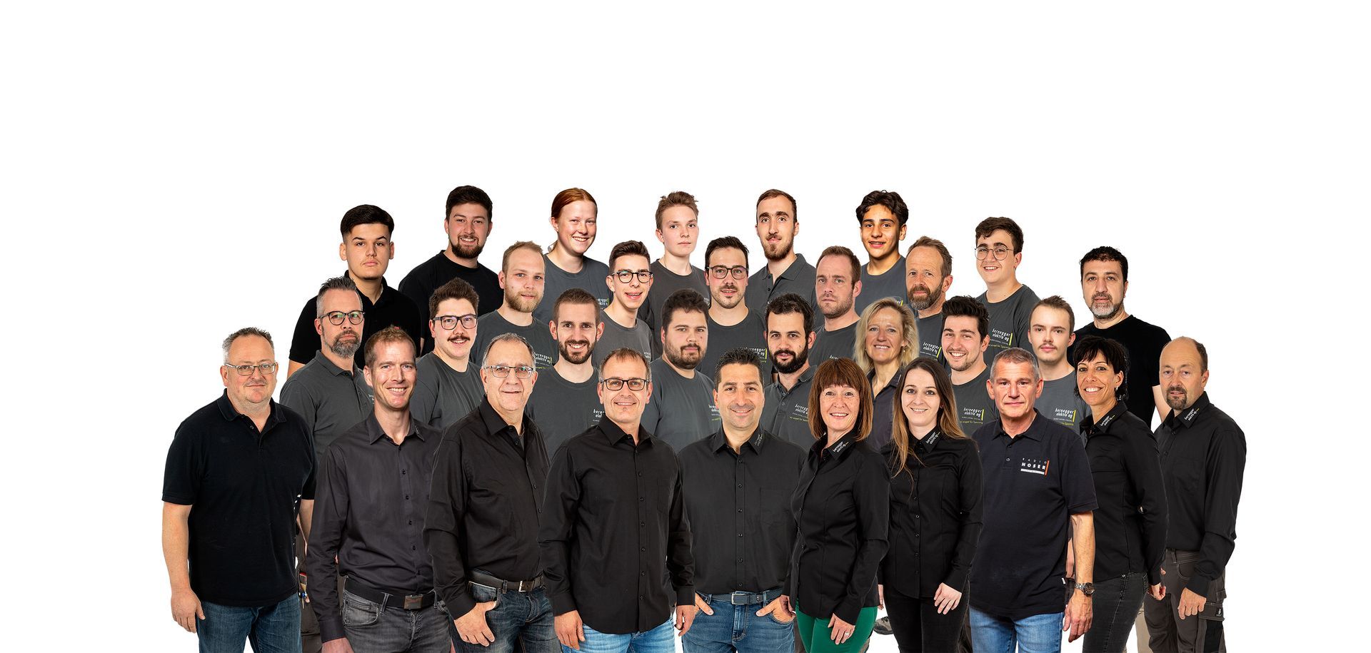 Eine Gruppe von Männern und Frauen, überwiegend in grauer und schwarzer Kleidung, posiert vor einem weißen Hintergrund.