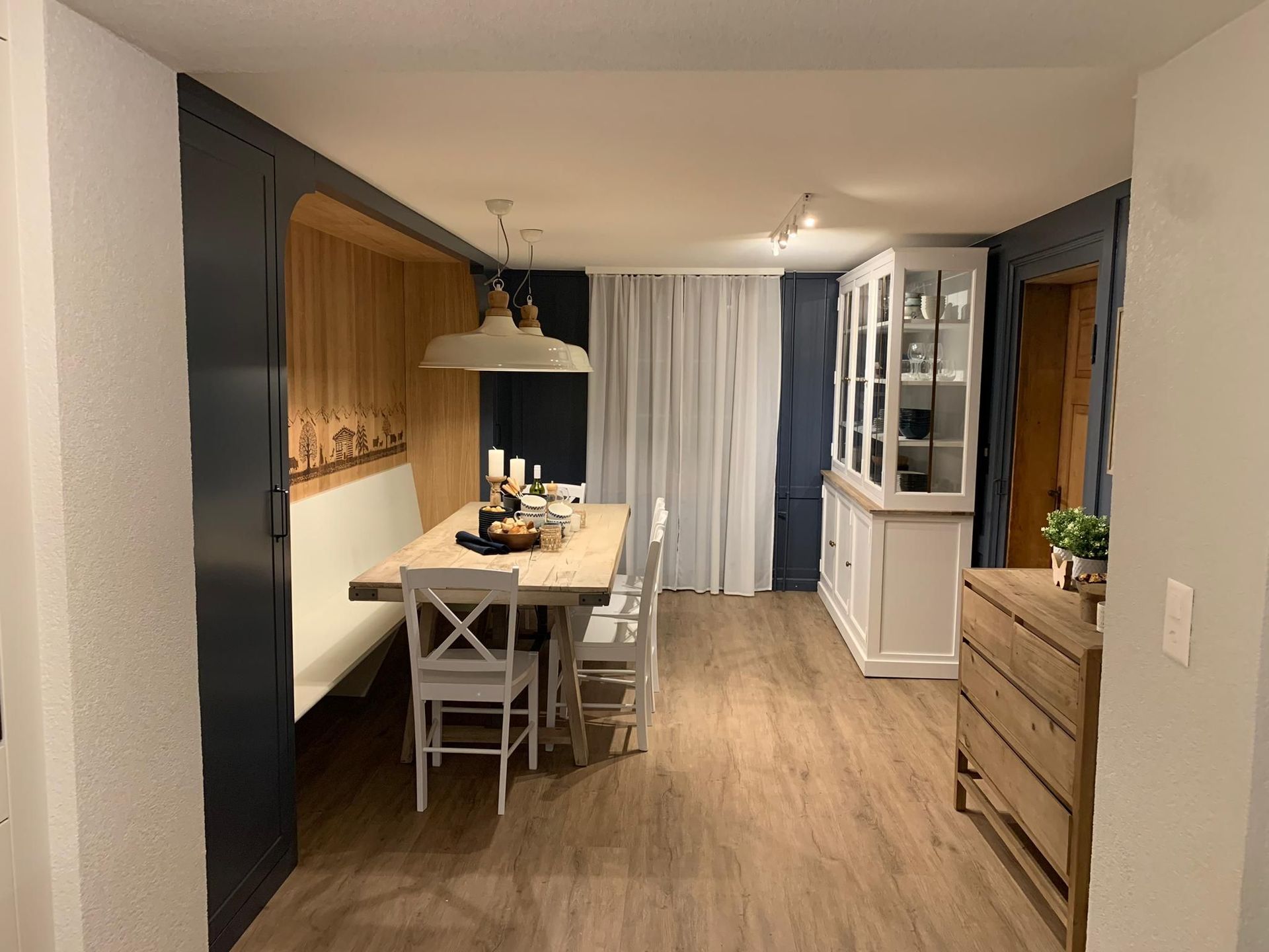 Gemütliches Esszimmer mit Holzboden, eingebauter Bank, Esstisch mit Stühlen und weißem Schrank.