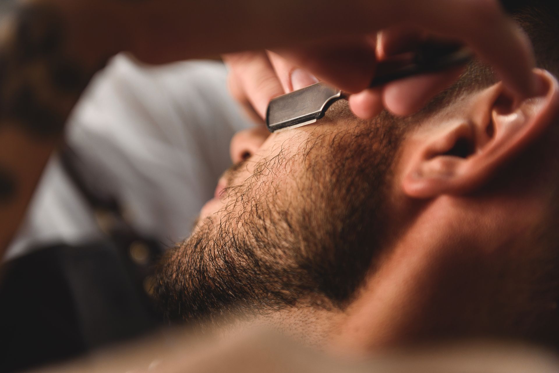 Un hombre se está afeitando la barba con una navaja por un barbero.