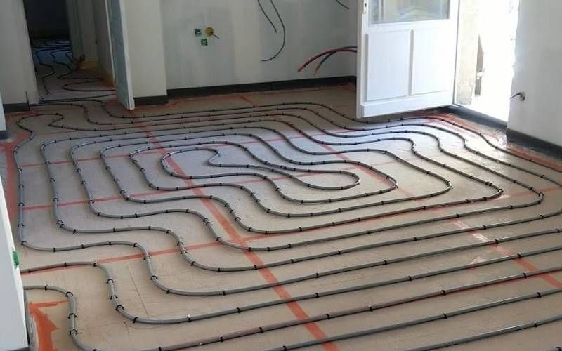 Sol avec des tuyaux de chauffage en serpentin posés avant l’installation du sous-plancher, dans une pièce en cours de rénovation