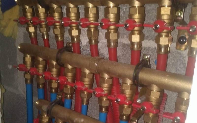 Collecteur de plomberie équipé de plusieurs vannes en laiton et de tuyaux rouges et bleus dans un local technique