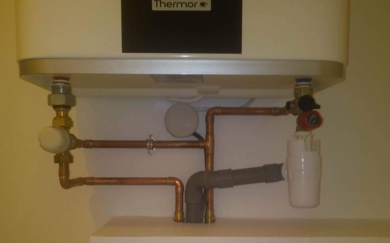 Tuyauterie sous évier et installation d’un filtre à eau sous un appareil blanc, avec des tuyaux en cuivre et une bouteille suspendue