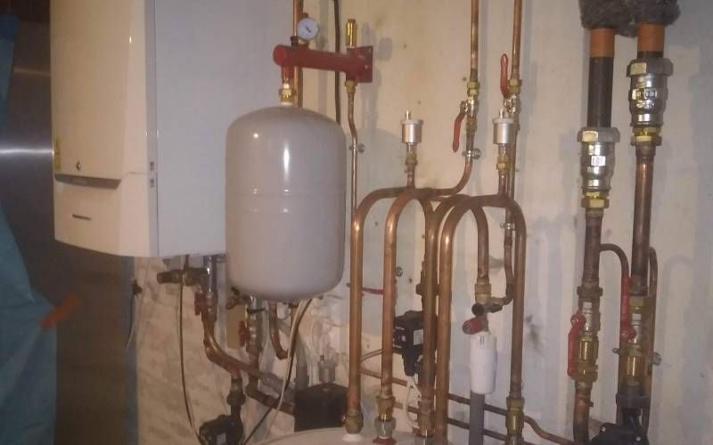 Chaufferie avec un vase d’expansion gris, des tuyaux, des vannes et un chauffe-eau mural