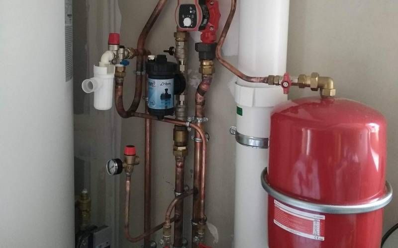 Local technique avec un vase d’expansion rouge, des tuyaux, des vannes et des équipements de chauffage fixés au mur