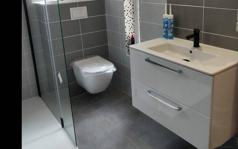 Salle de bains moderne avec toilettes suspendues, douche vitrée et meuble vasque blanc sur un sol carrelé gris