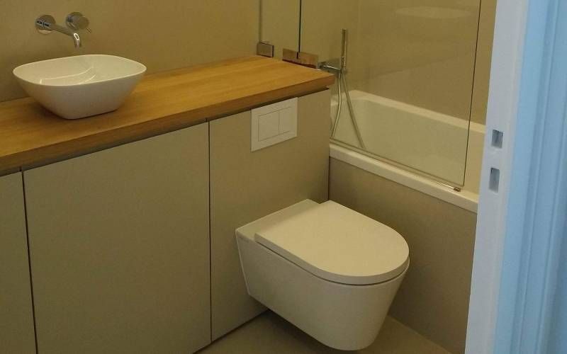 Petite salle de bains avec toilettes suspendues, lavabo, plan de travail en bois et baignoire