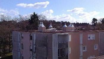 Immeuble d’habitation sous un ciel bleu nuageux, aperçu au-dessus d’arbres dénudés