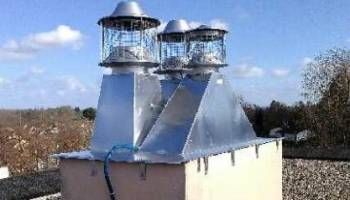 Système de ventilation sur le toit avec deux cheminées métalliques et des conduits bleus sur fond de ciel nuageux