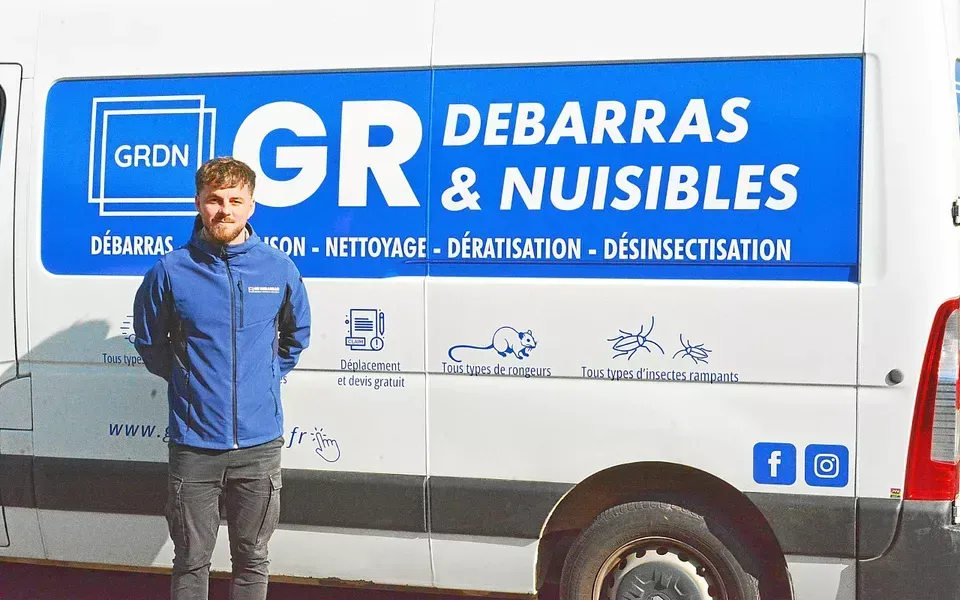 Un homme en veste bleue se tient à côté d'une camionnette portant le logo de l'entreprise « GR Débarras & Nuisibles ».