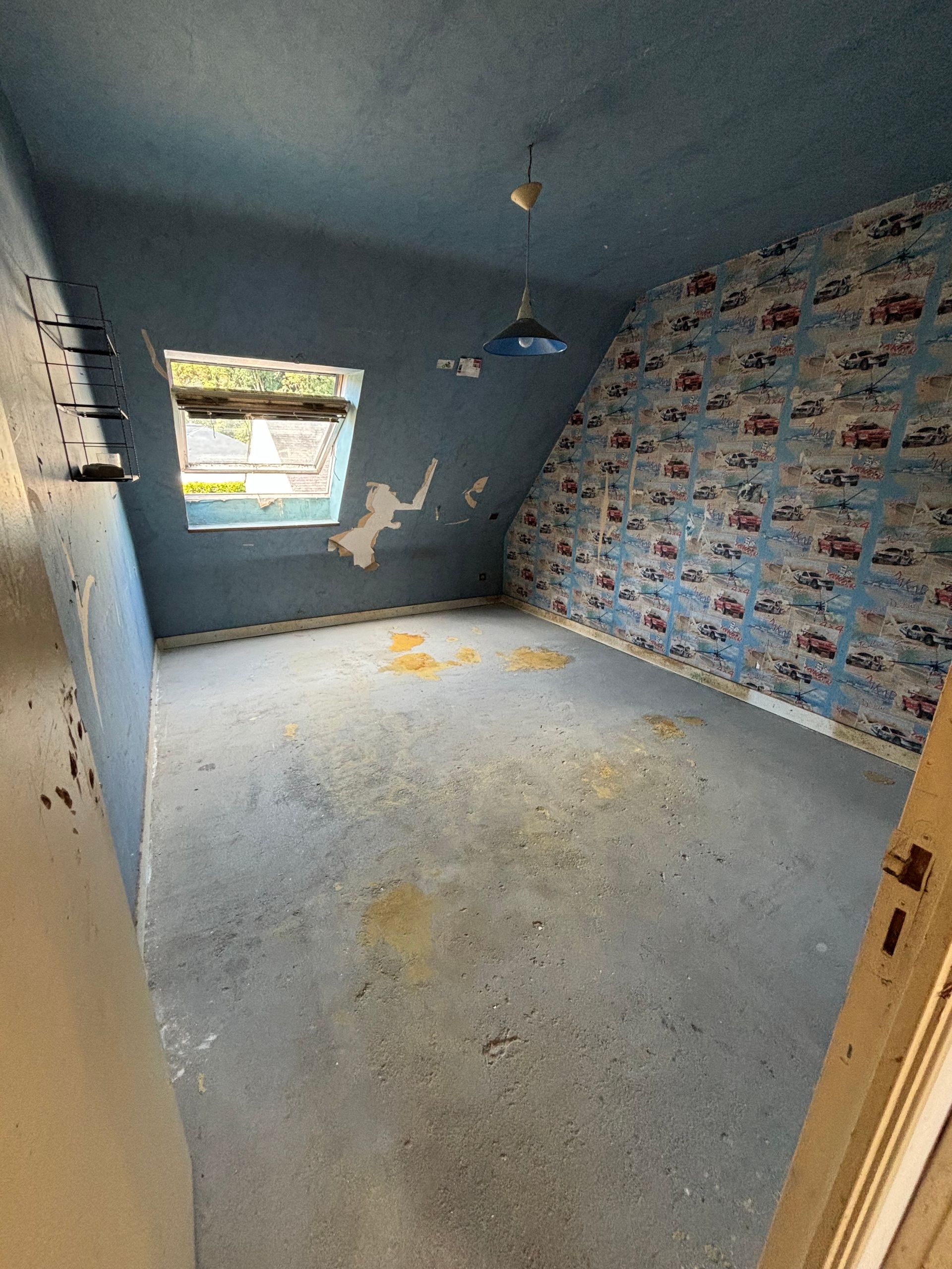 Pièce vide avec plafond bleu en pente, papier peint à motifs et fenêtre.