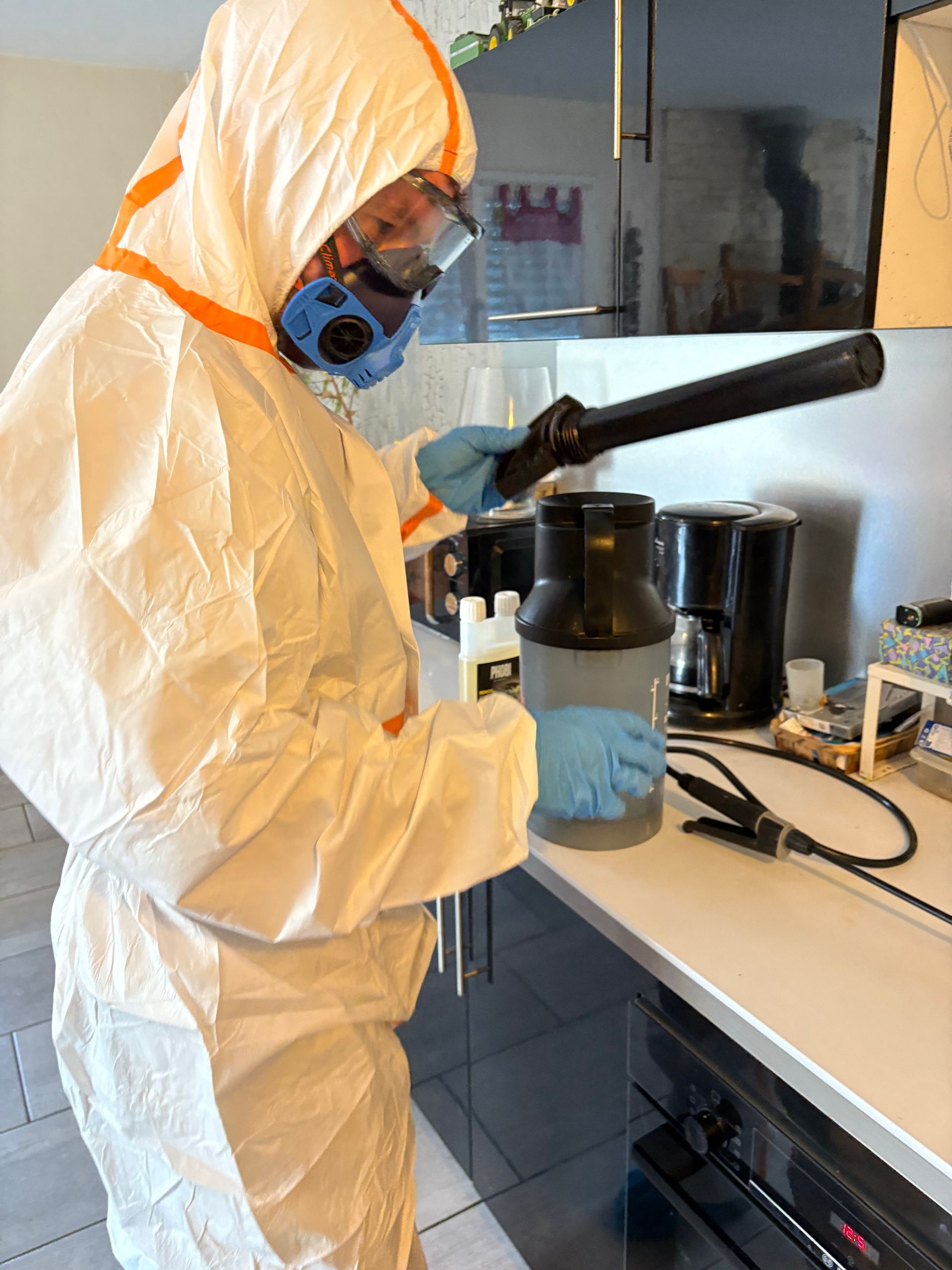 Une personne en combinaison de protection pulvérise un insecticide près d'une bouche d'aération métallique.