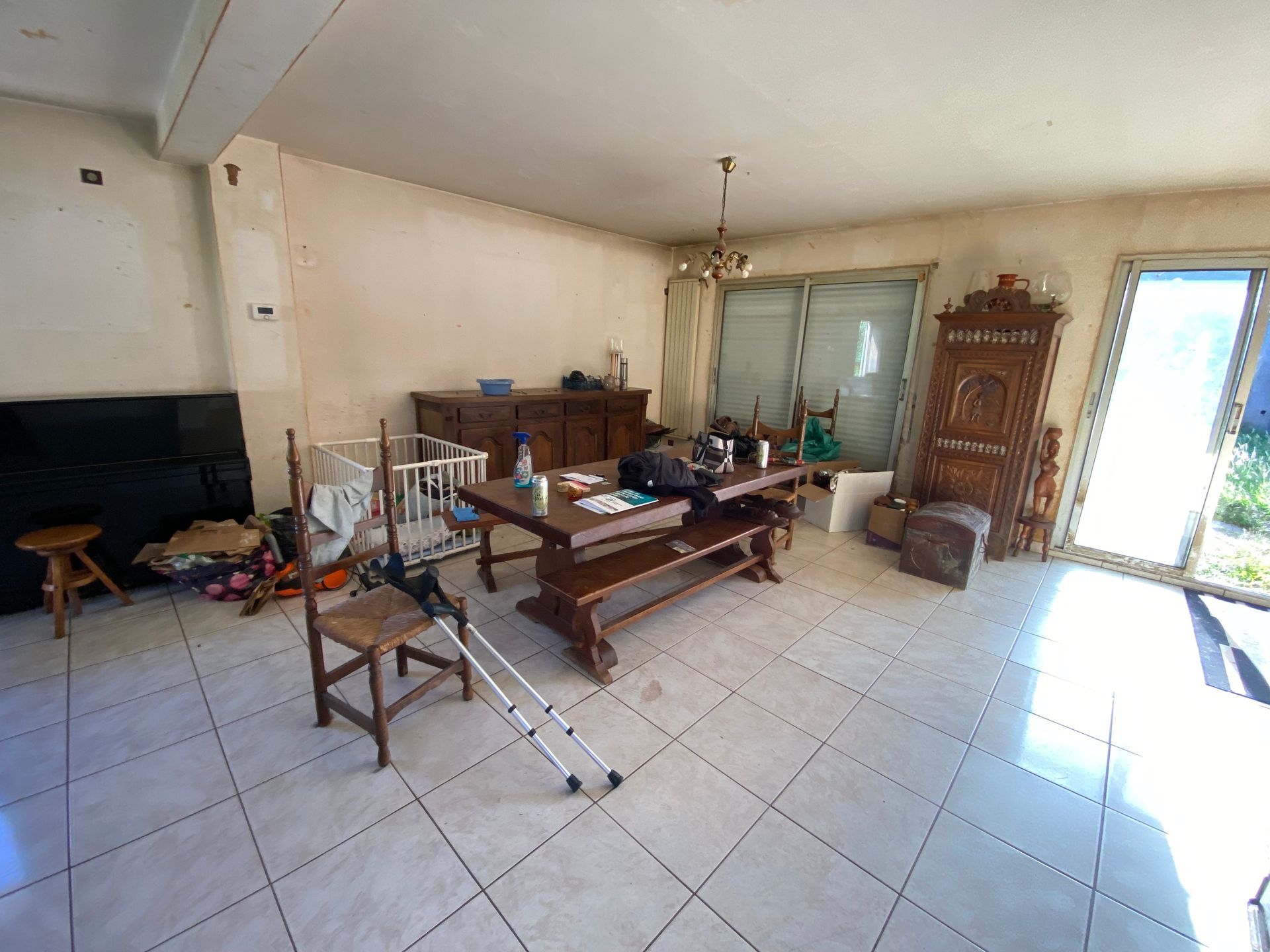 Un salon meublé avec parcimonie, comprenant une table à manger, des chaises et des béquilles sur un sol carrelé.