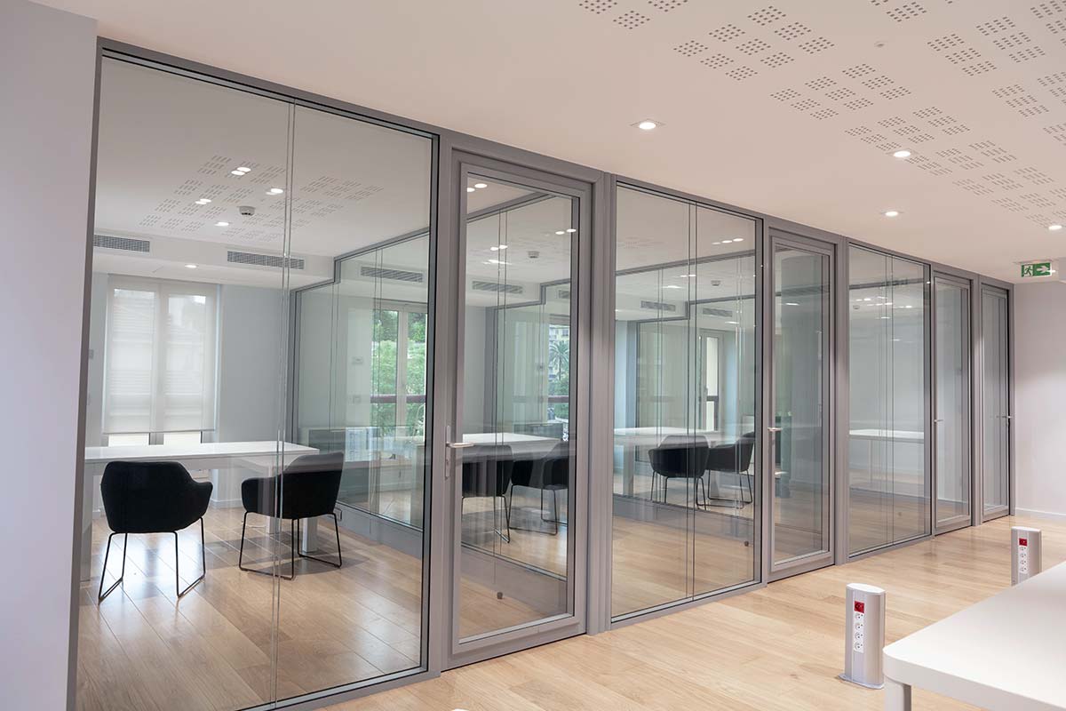 Plusieurs bureaux d'une entreprise dont les séparations sont uniquement faites de vitres et portes transparentes