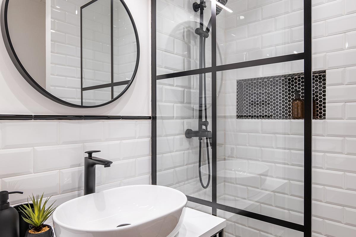 Paroi de douche en verre avec un encadrement noir dans une salle de bains en briques blanches