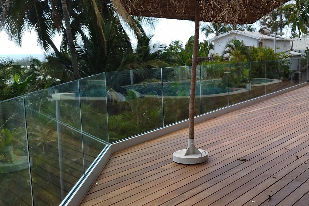 Garde-corps en verre sur une terrasse en bois sur fond de multiples palmiers