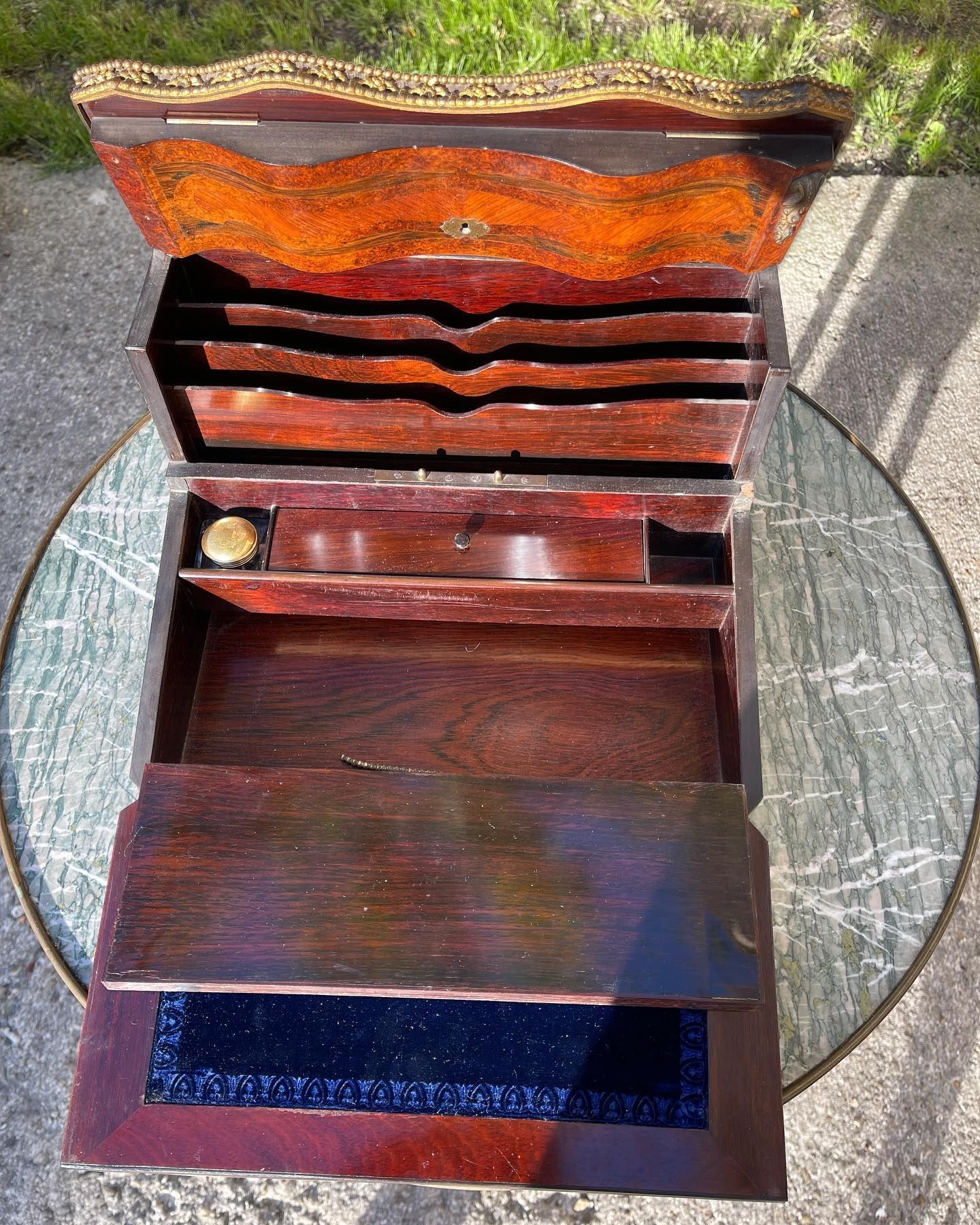 Bureau ancien en bois, ouvert, laissant apparaître des compartiments et un encrier sur une table en marbre.