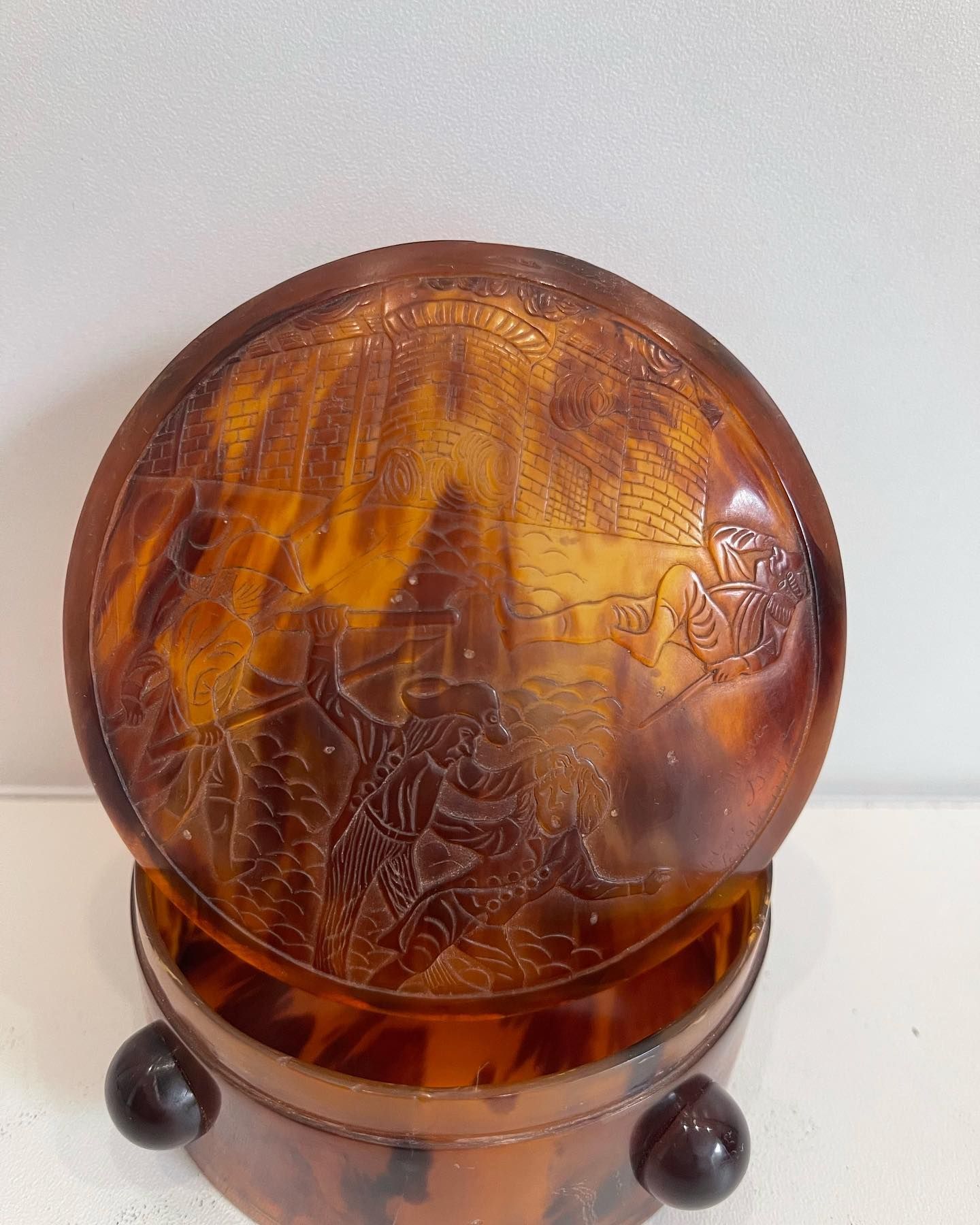 Boîte en écaille brune ornée d'un paysage sculpté, soutenue par trois petites sphères sombres.