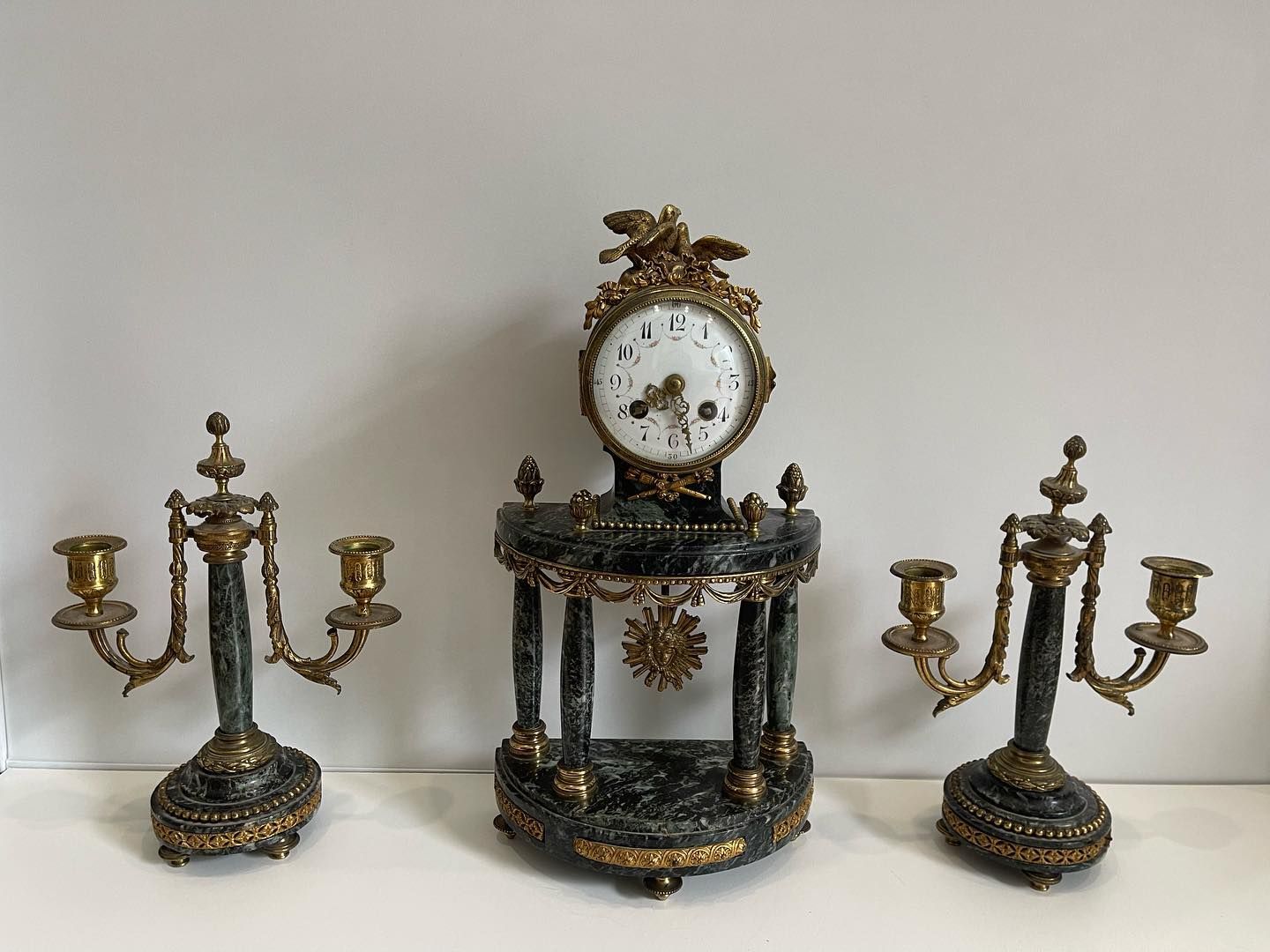 Horloge ancienne avec deux candélabres assortis. L'horloge possède un cadran rond et repose sur un socle en marbre.