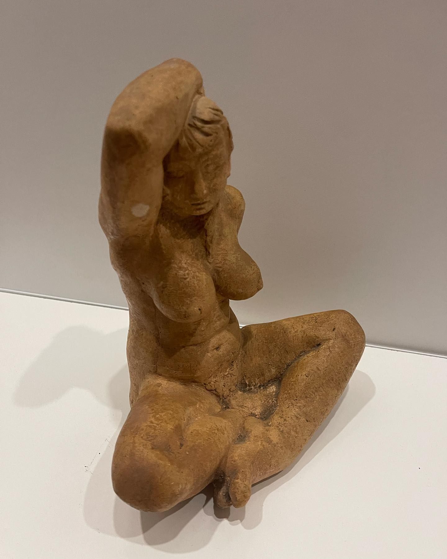 Sculpture d'une figure nue assise, les bras levés, en terre cuite.