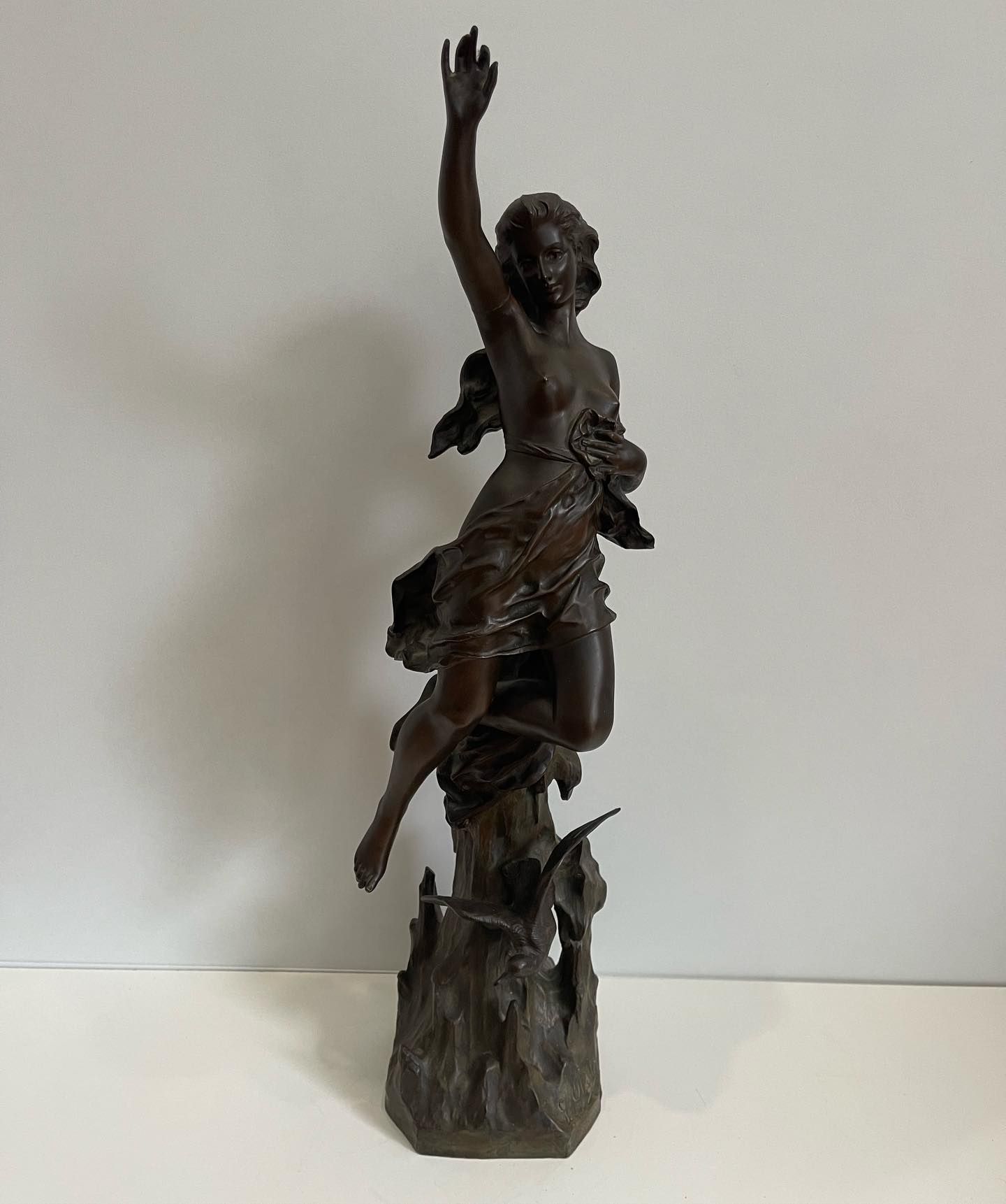 Sculpture en bronze d'une femme au bras tendu, sur un socle texturé.