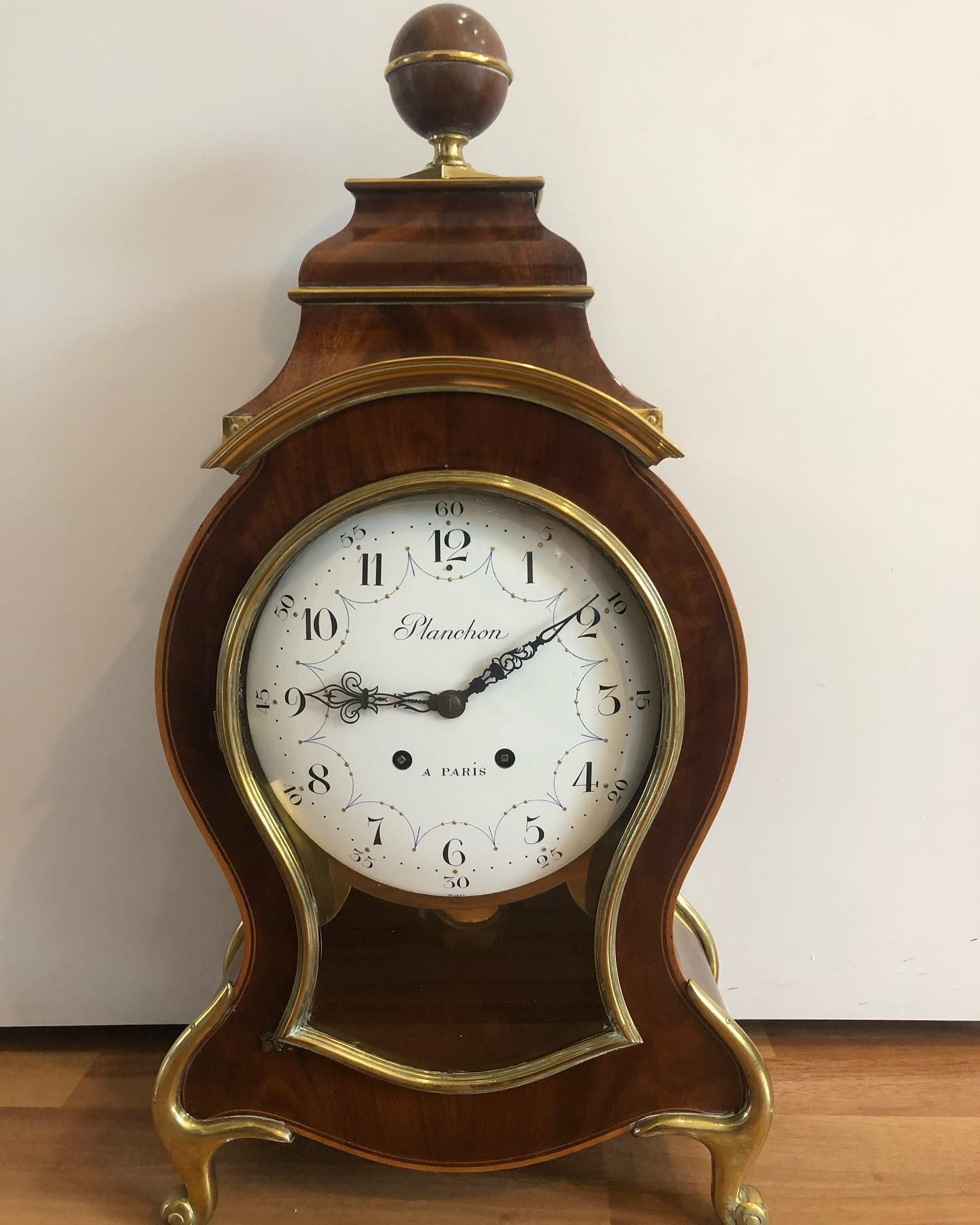 Pendule de cheminée en bois avec cadran blanc, ornements en laiton et fleuron en bois.