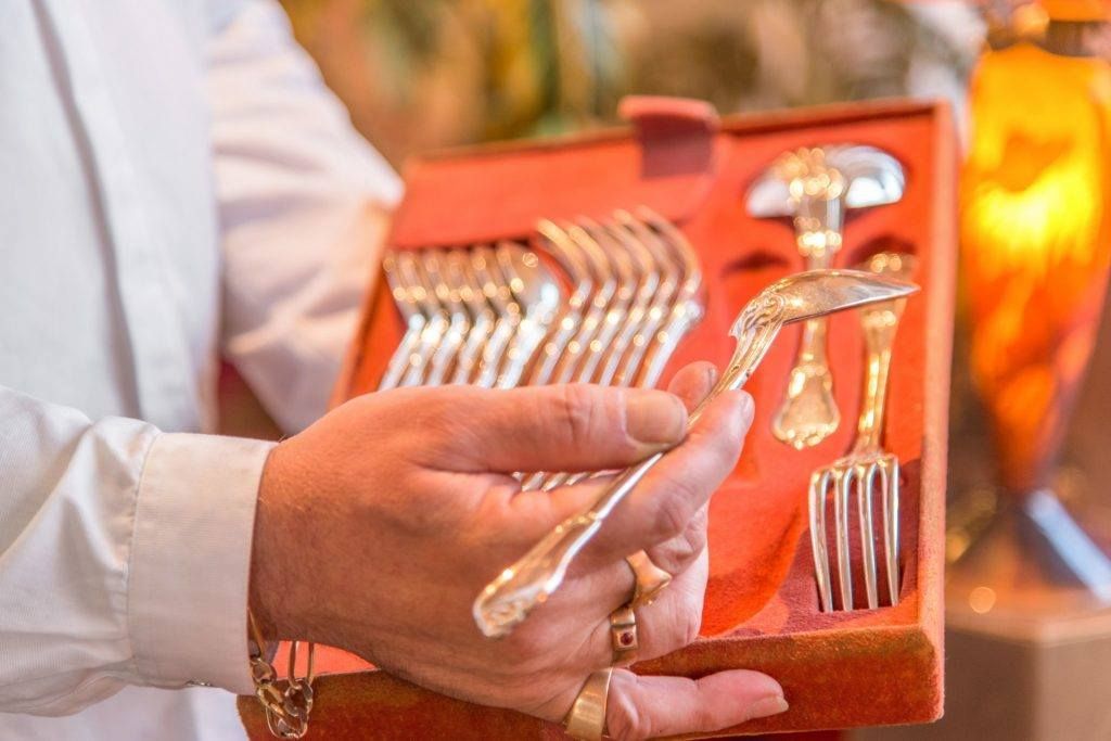 Personne tenant un coffret de couverts en argent, examinant une fourchette. Étui en velours rouge, chemise blanche.