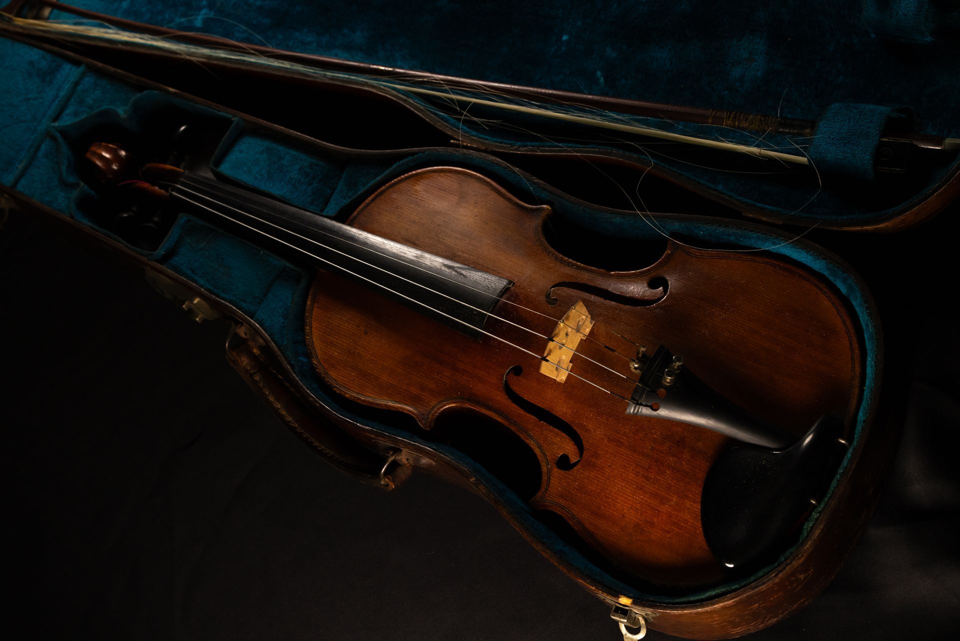 Violon dans un étui ouvert doublé de bleu, archet posé à côté ; instrument en bois foncé à la finition brun doré.