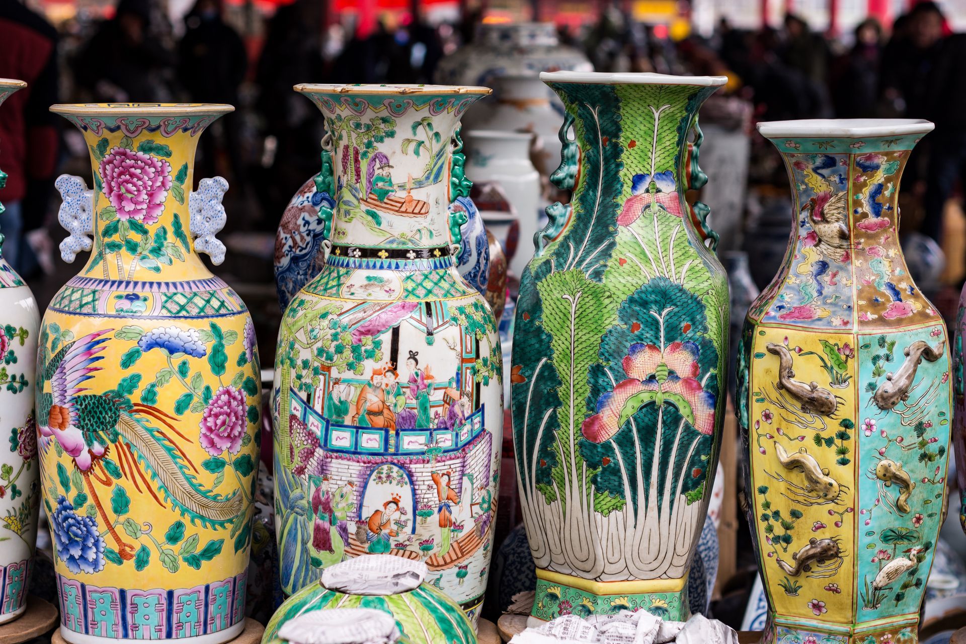 Quatre vases chinois colorés et richement décorés de motifs floraux et de scènes, probablement destinés à la vente sur un marché.