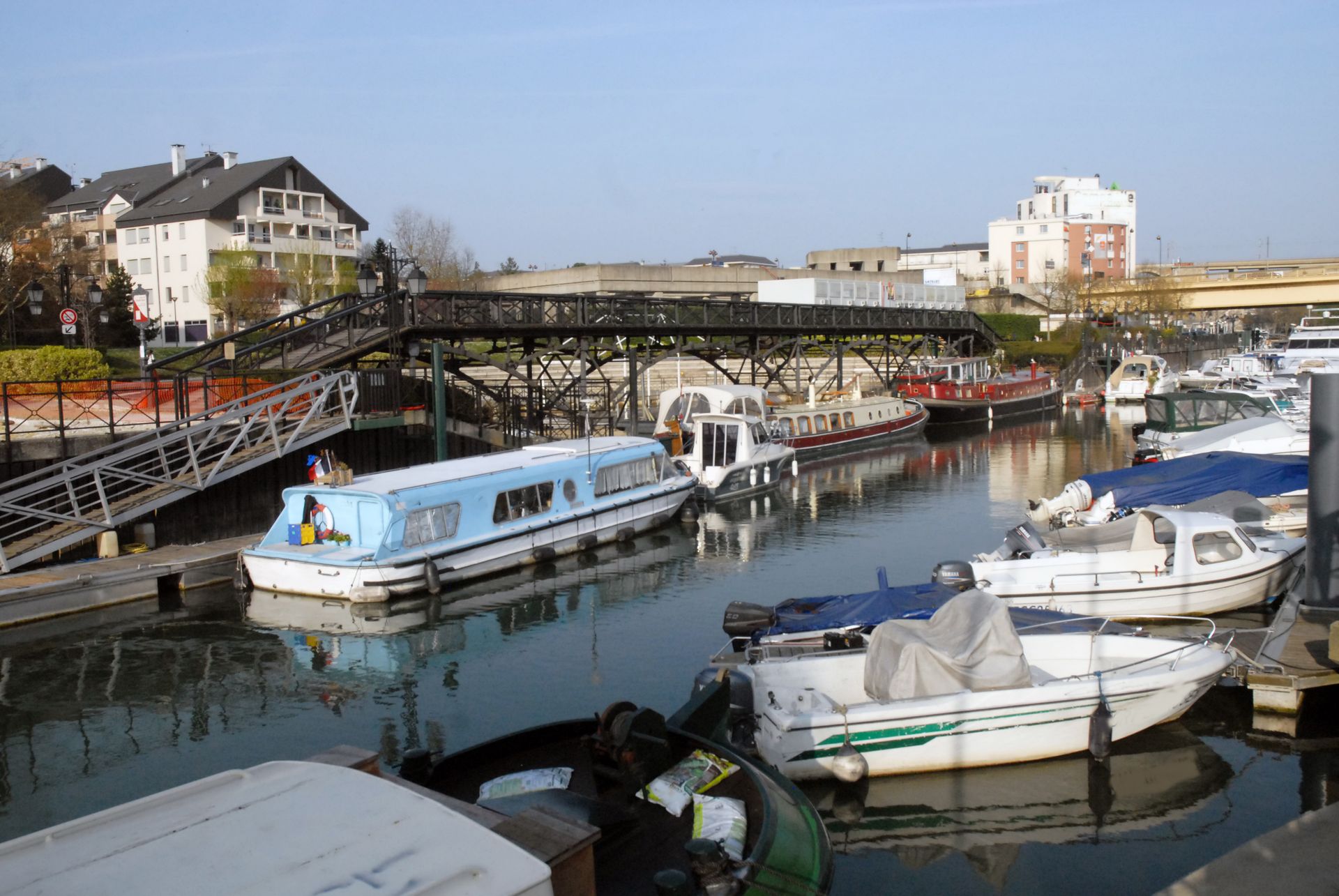 Des bateaux amarrés dans un port, avec un pont au-dessus et des bâtiments en arrière-plan, par une journée ensoleillée.