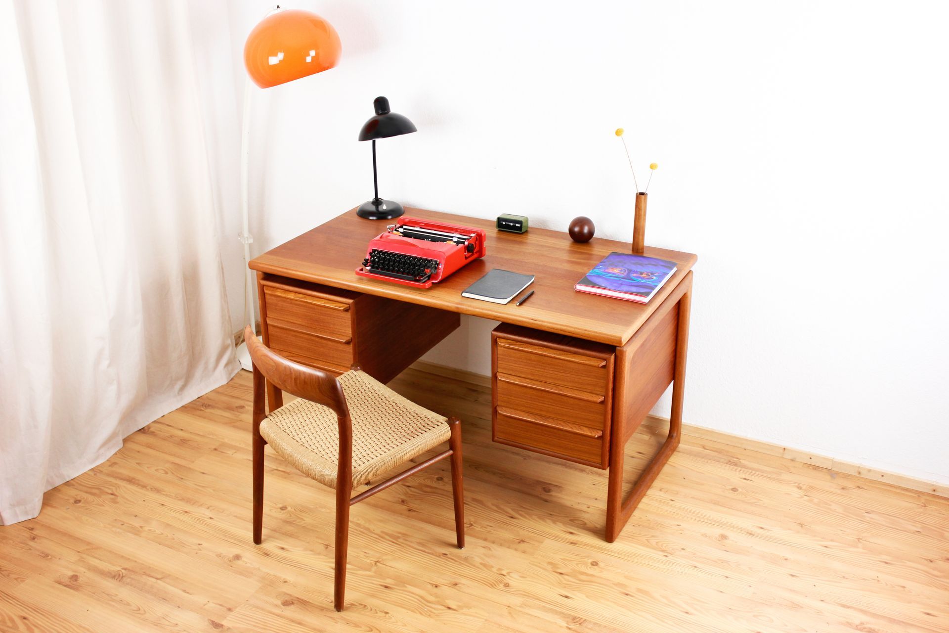 Un bureau en bois avec une machine à écrire, une lampe et une chaise dans une pièce avec une fenêtre.