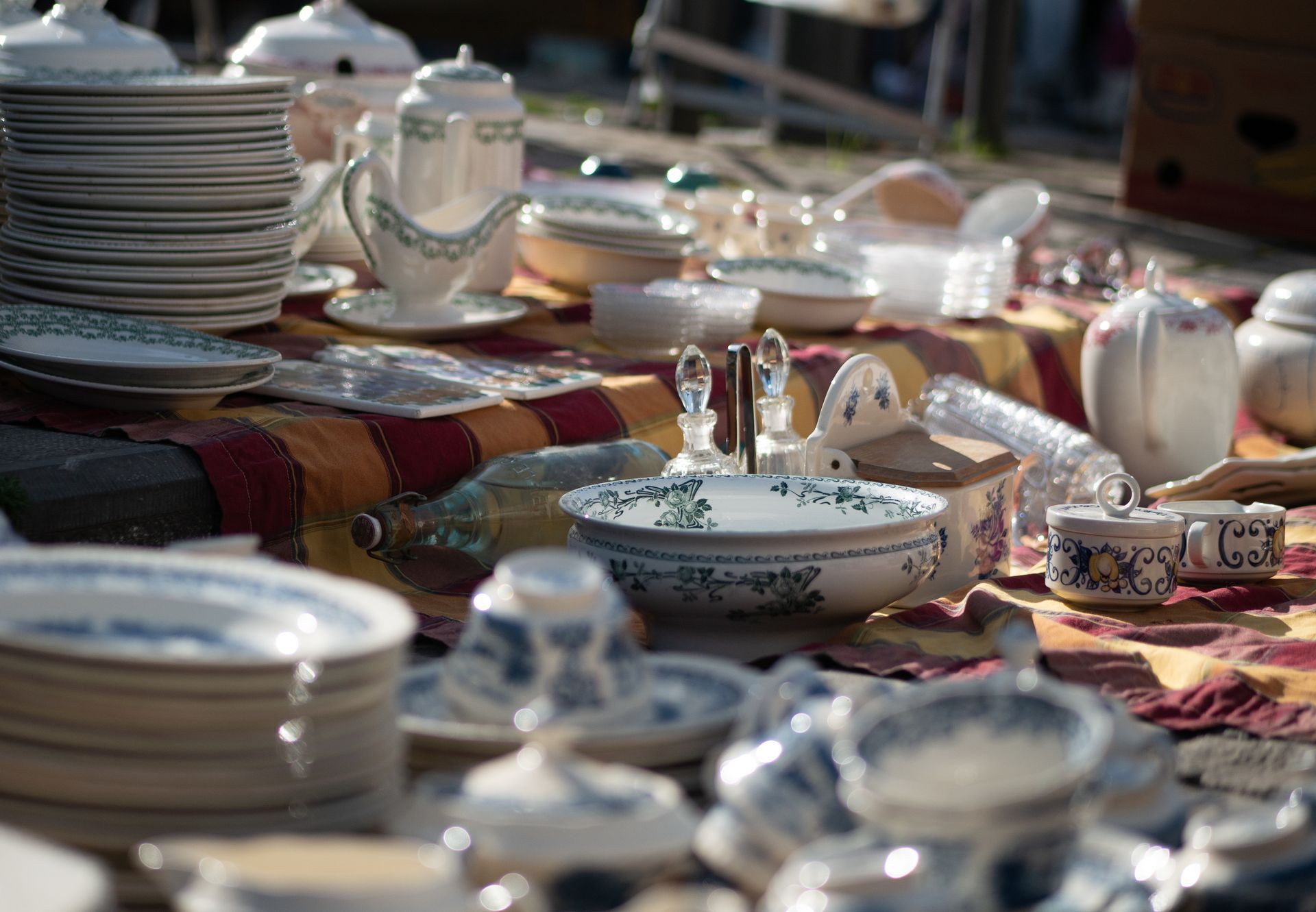Présentation de vaisselle ancienne sur une nappe à motifs ; motifs floraux blancs et bleus.