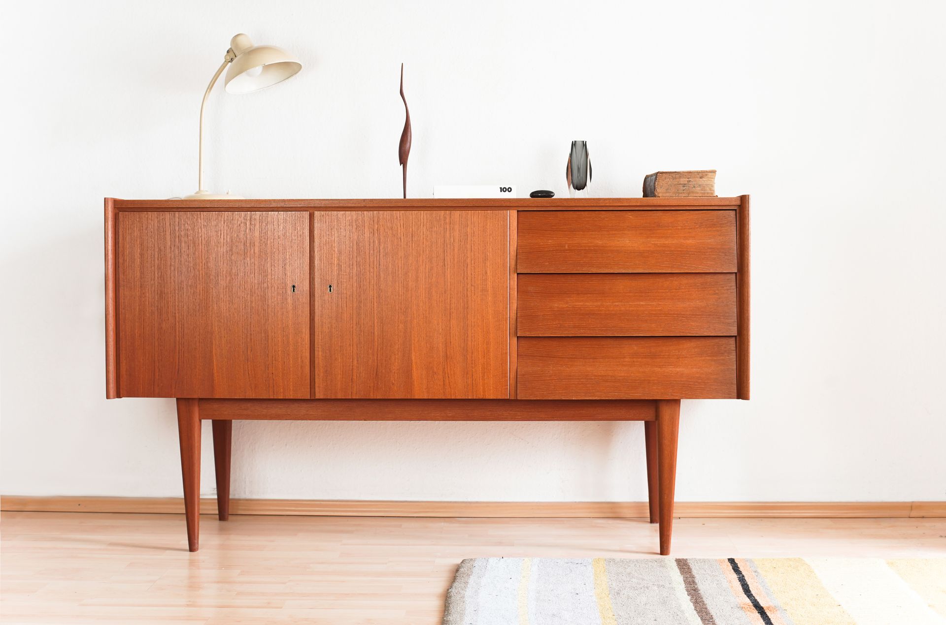 Pièce avec piano ancien, fauteuil, tableaux encadrés et petite table. Murs, rideaux et carrelage aux tons neutres.