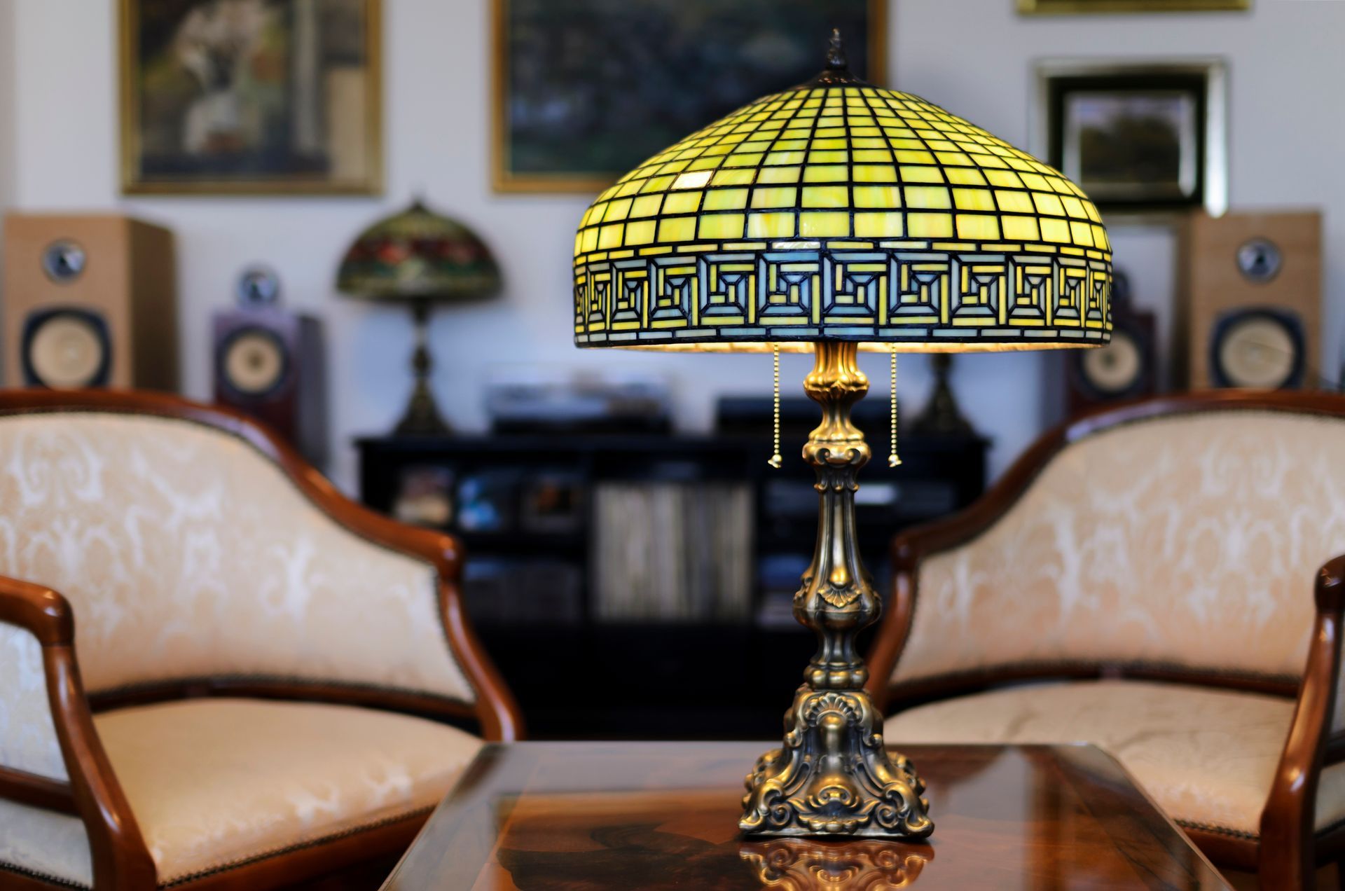 Lampe de style Tiffany sur une table, entre deux chaises, intérieur avec œuvres d'art et haut-parleurs en arrière-plan.