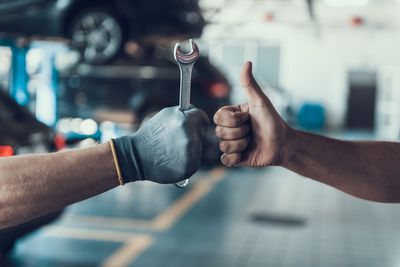 Deux ouvriers gantés se font un check autour d'une clé à molette dans un atelier automobile.