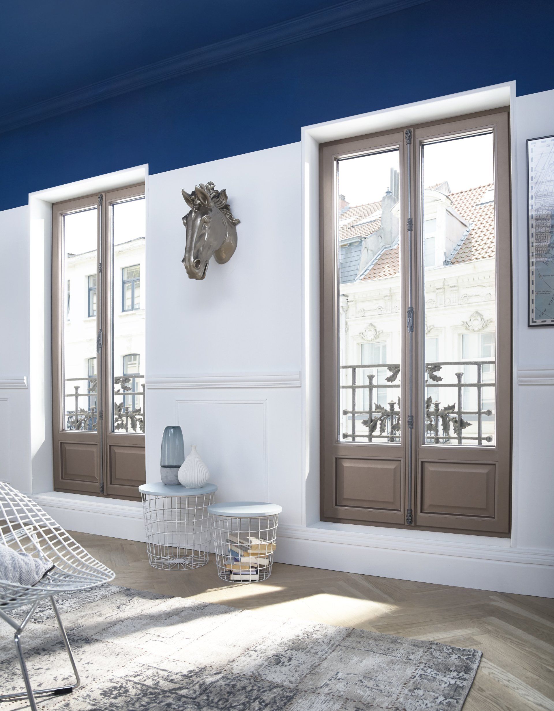Int&eacute;rieur avec deux fen&ecirc;tres &agrave; cadre marron donnant sur une ville, murs blancs et plafond bleu.