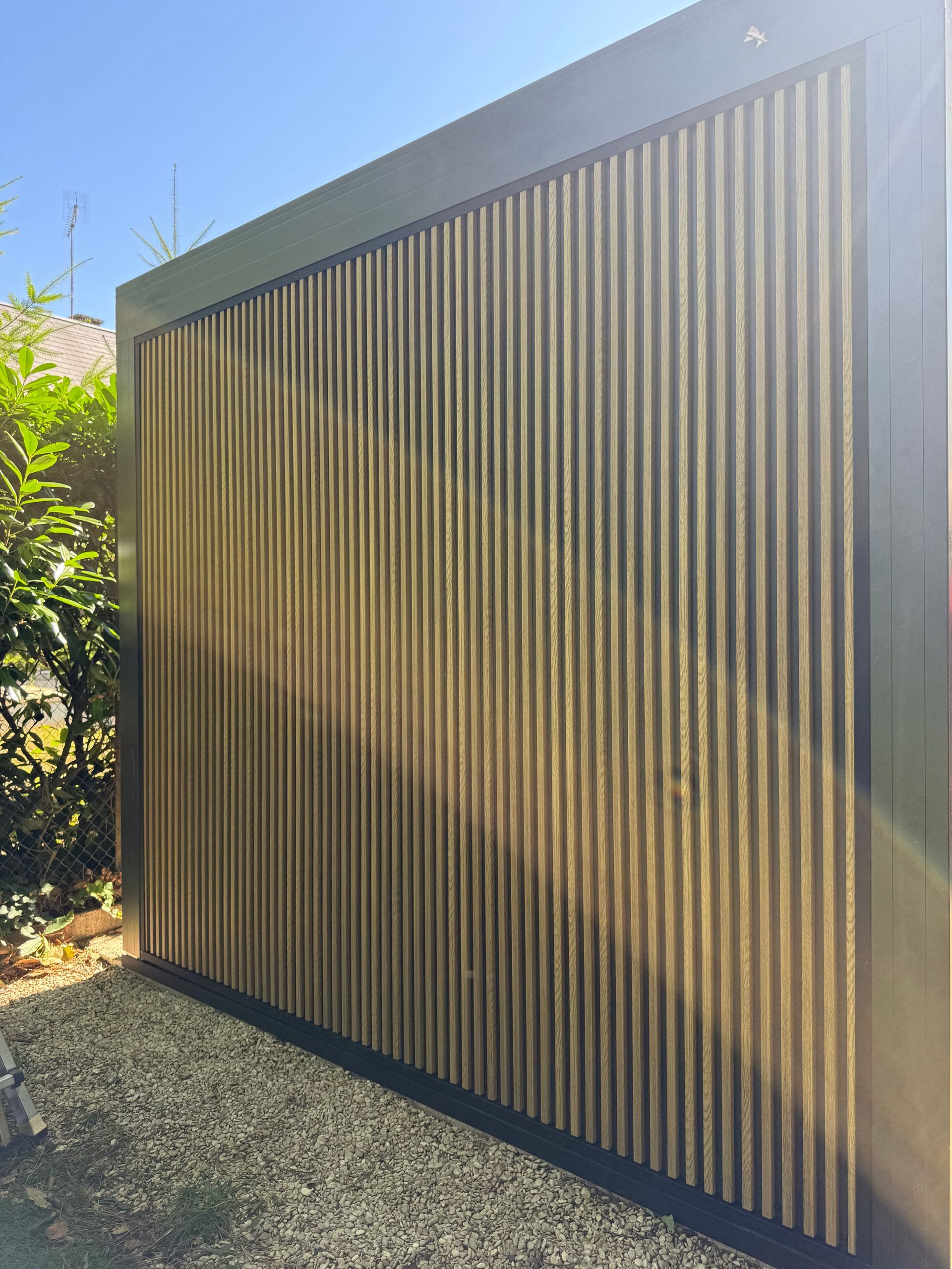 Clôture d'intimité en lattes de bois avec cadre foncé, sur gravier, à l'extérieur.