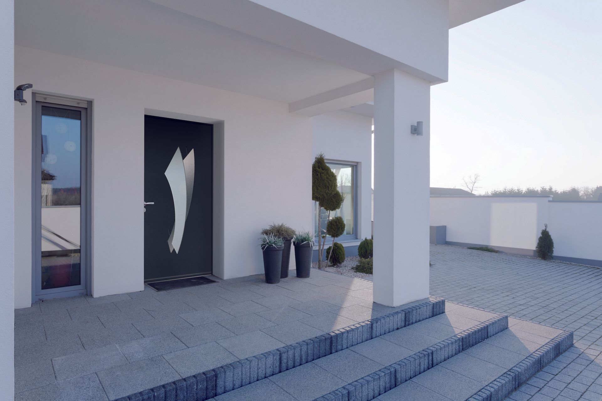 Une entrée moderne avec une porte noire ornée d'un motif graphique blanc, des marches grises et une façade de maison blanche.