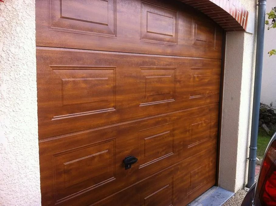 Porte de garage sectionnelle marron à motif de grain de bois, avec panneaux rectangulaires et poignée centrale noire.