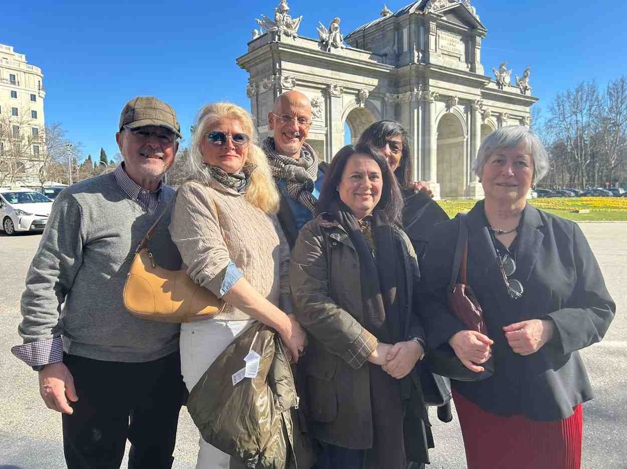 Un grupo de cinco personas posa frente al monumento de la Puerta de Alcalá en Madrid en un día soleado.
