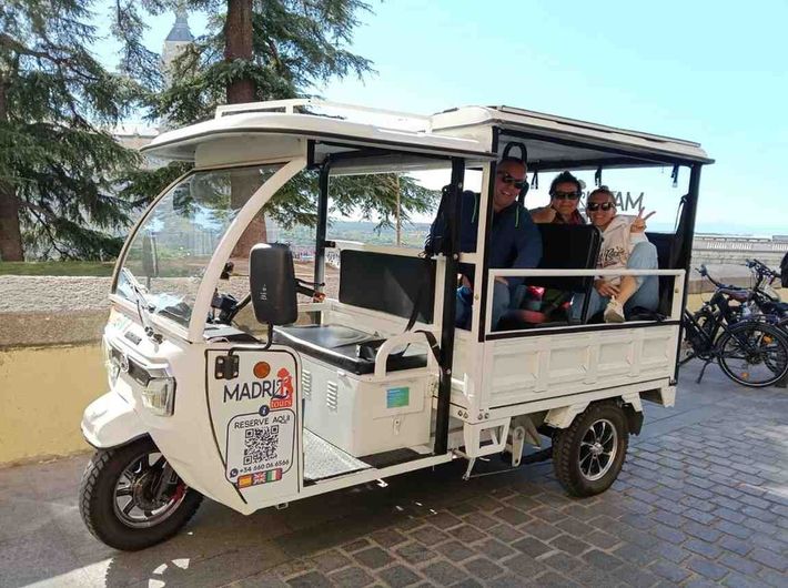 Tres personas sonríen mientras viajan en un tuk-tuk eléctrico blanco de tres ruedas, descapotable.