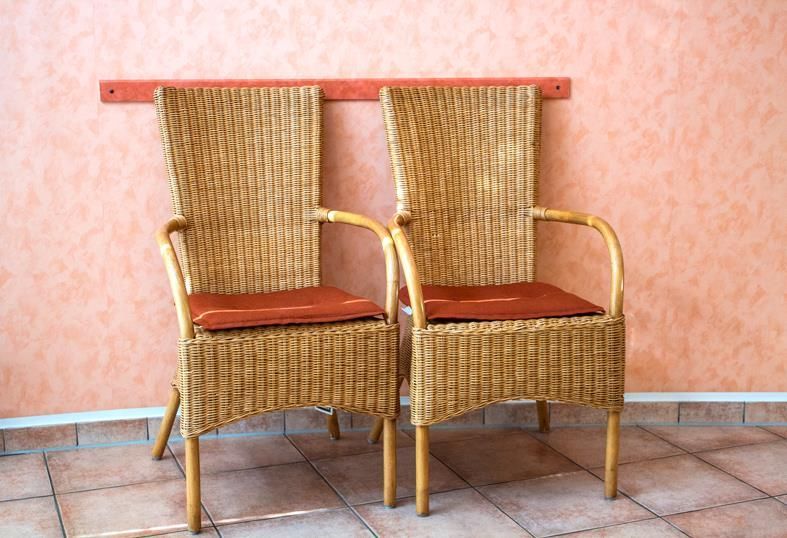 Zwei Korbstühle stehen nebeneinander vor einer rosa Wand.