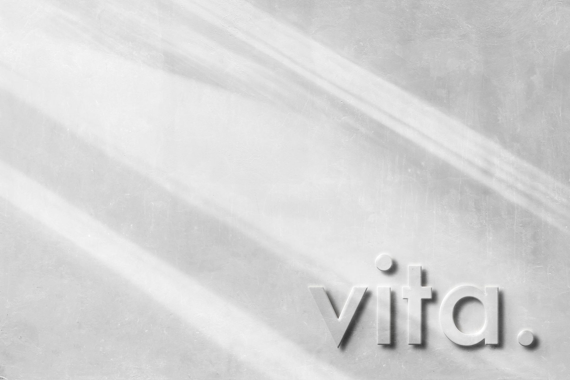 Heller, minimalistischer Hintergrund mit weichen Lichtreflexen und dem Schriftzug „vita.“ in dezenter Prägung.