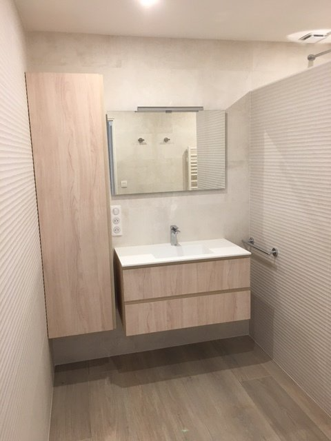 Petite salle de bains moderne avec meuble-lavabo mural, armoire à miroir et armoire de rangement en bois clair.