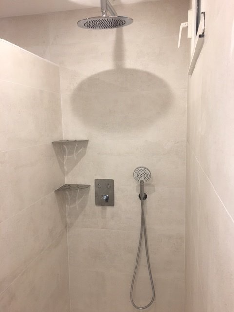 Douche minimaliste blanche avec pomme de douche effet pluie, douchette et étagère murale pour le savon.