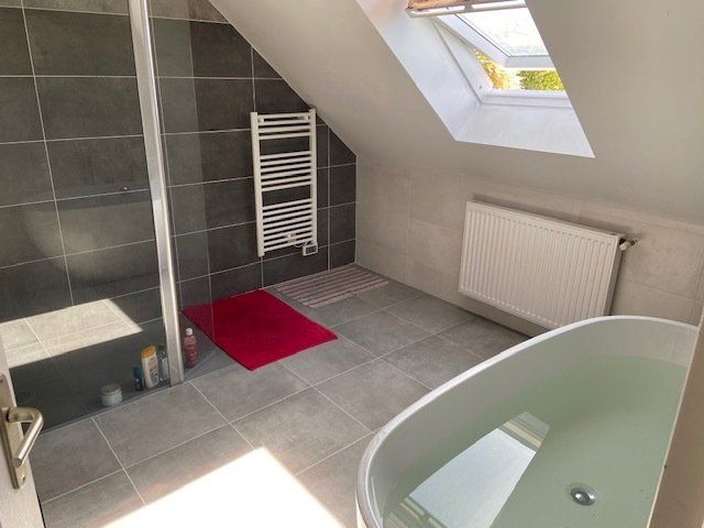 Salle de bains moderne avec baignoire, douche, puits de lumière, porte-serviettes et tapis de bain rouge.